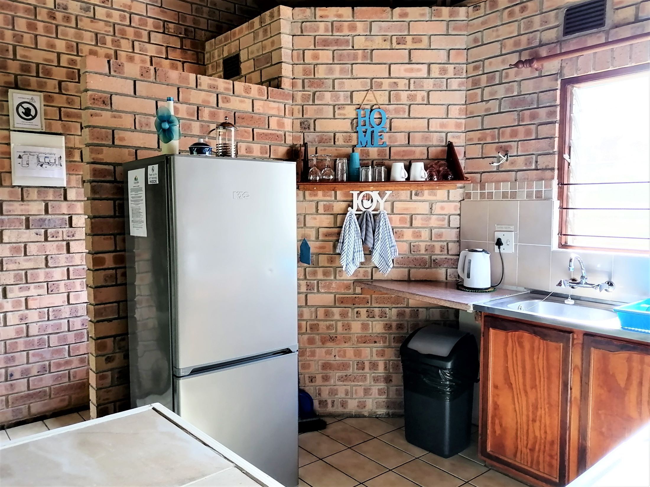 A kitchen with a brick wall, a refrigerator, a sink, and a trash bin.