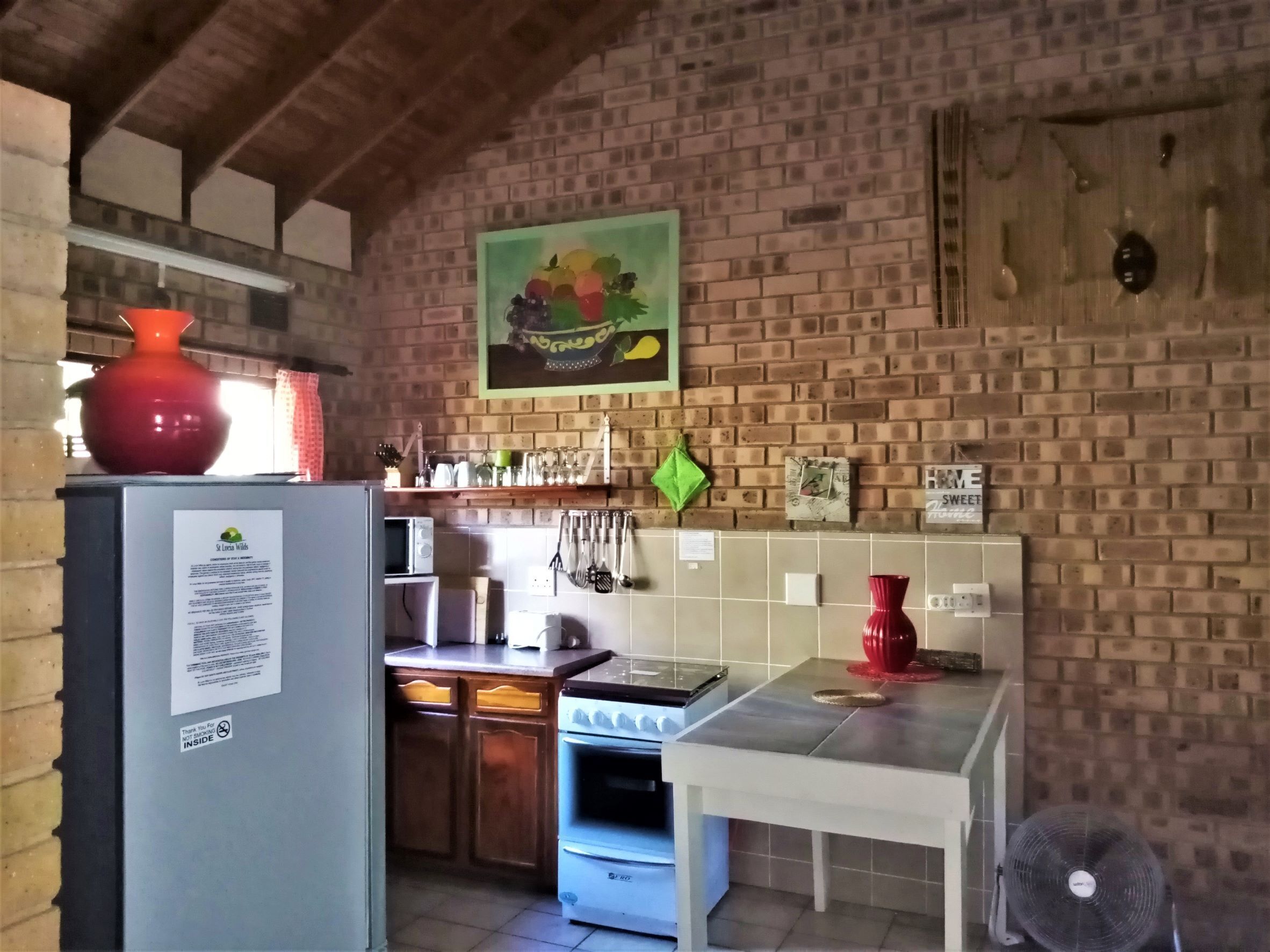 Uma cozinha com parede de tijolo, teto de madeira, geladeira, fogão e ventilador.