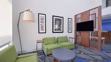 Habitación de hotel con sofá, una mesa redonda, televisión y cuadros en la pared.