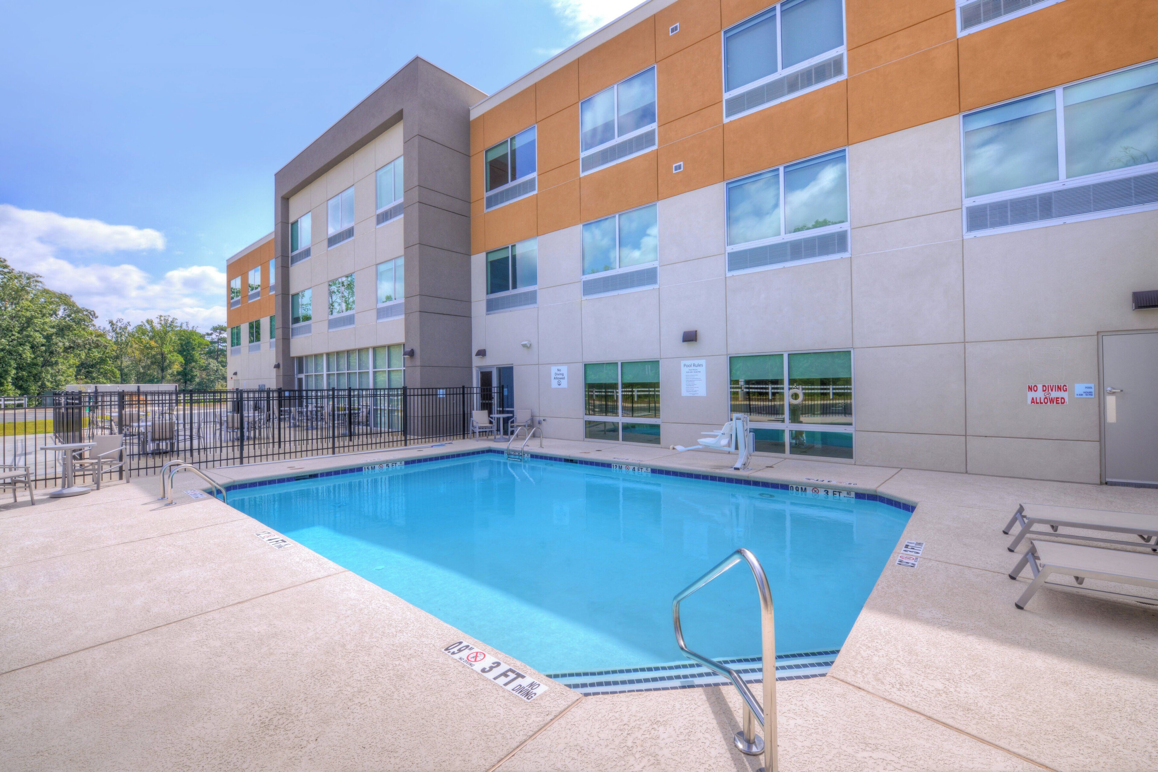 A modern building with a swimming pool, outdoor seating, and clear sky.