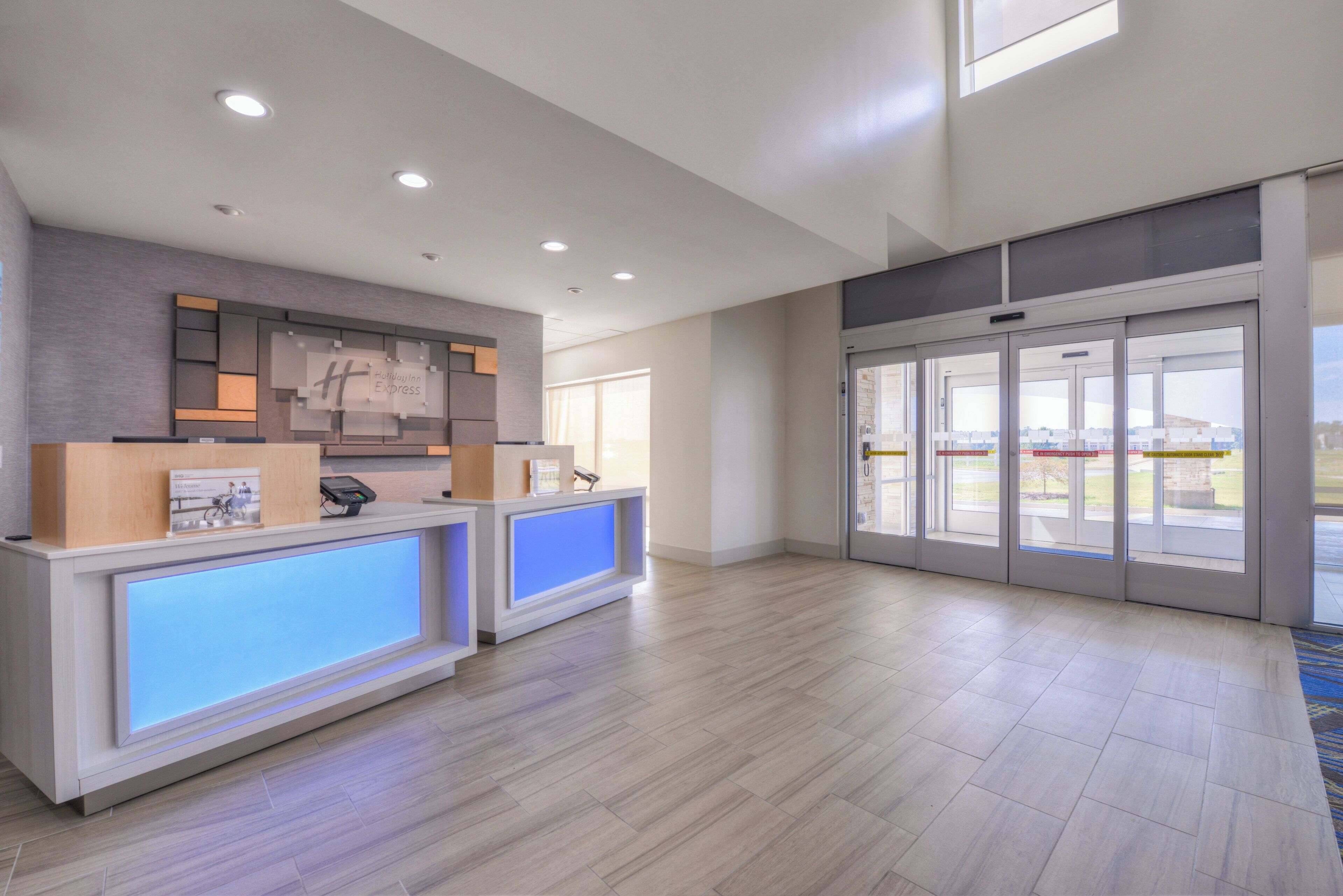 A hotel reception area with a modern design, featuring a reception desk, a digital display, and a glass door entrance.