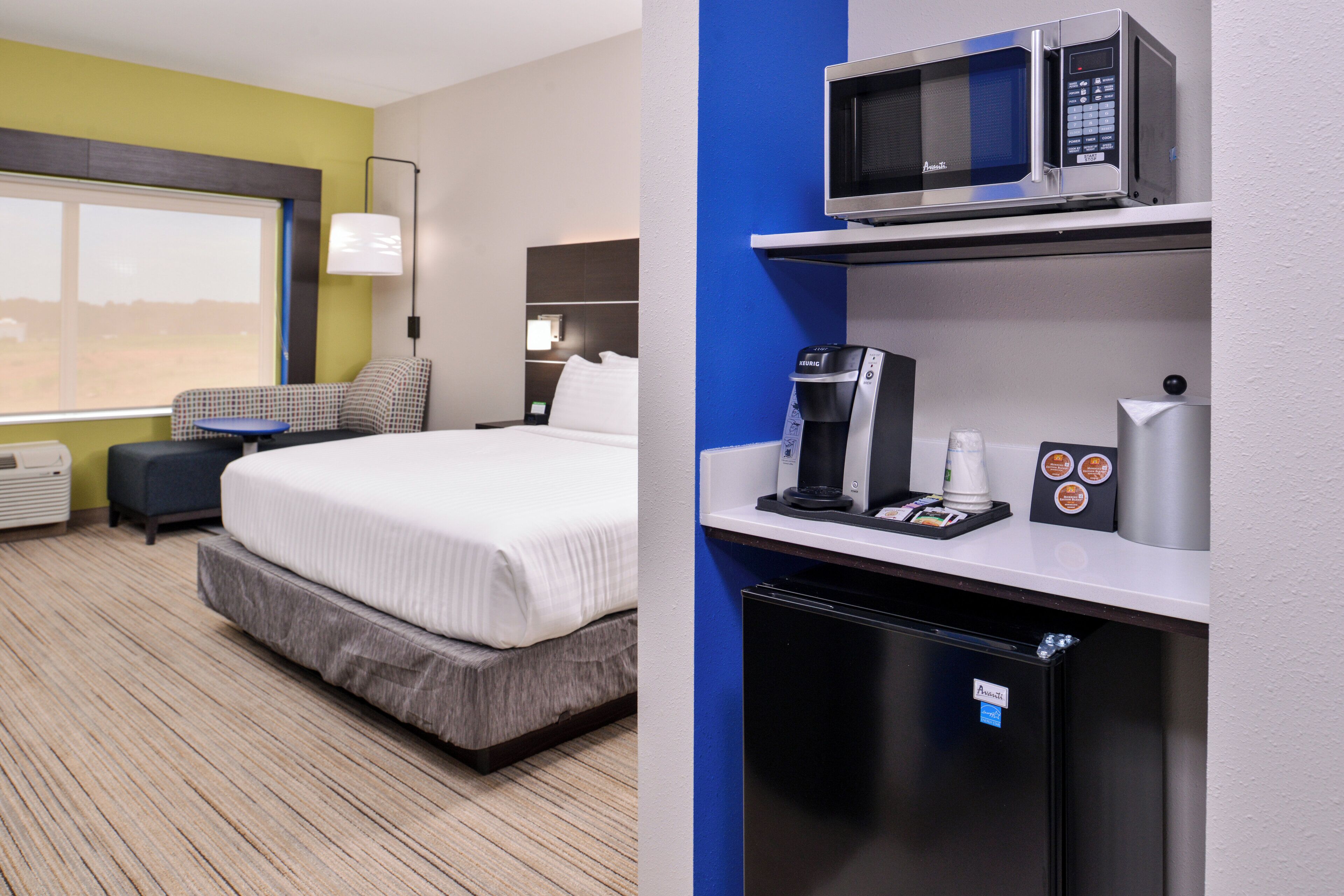 A hotel room with a bed, a minibar, a microwave, and a coffee machine.