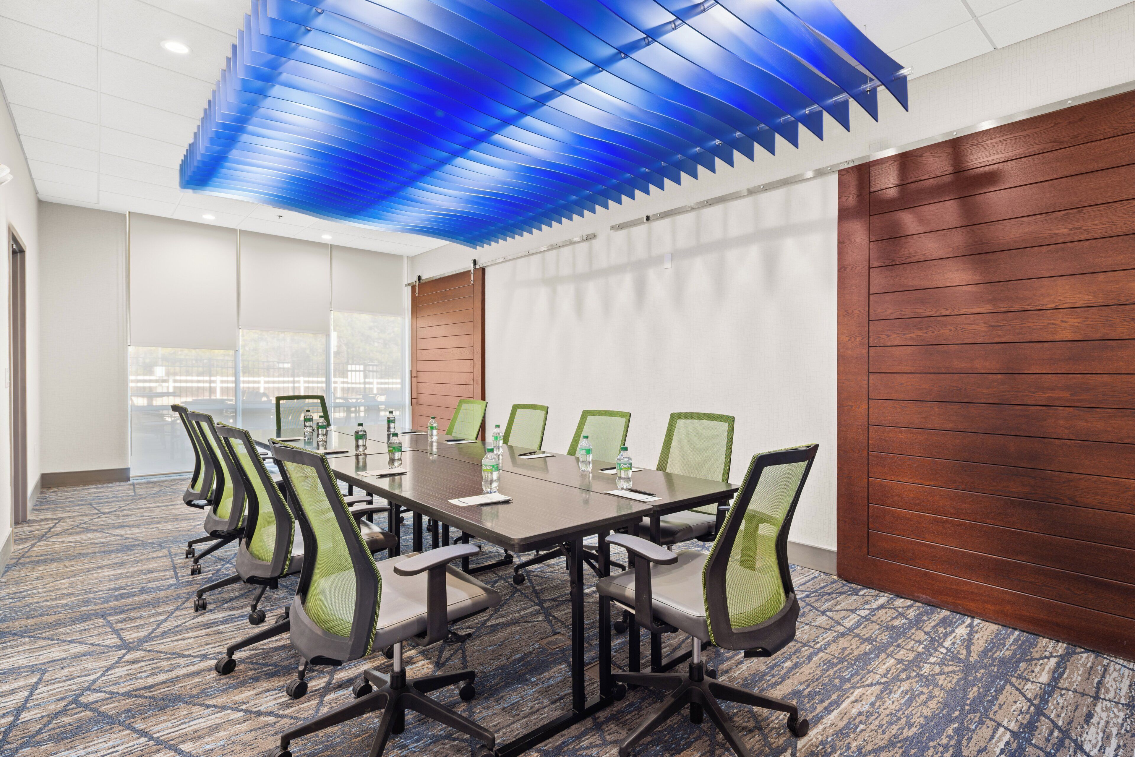A conference room with a long table, green chairs, and a blue ceiling.