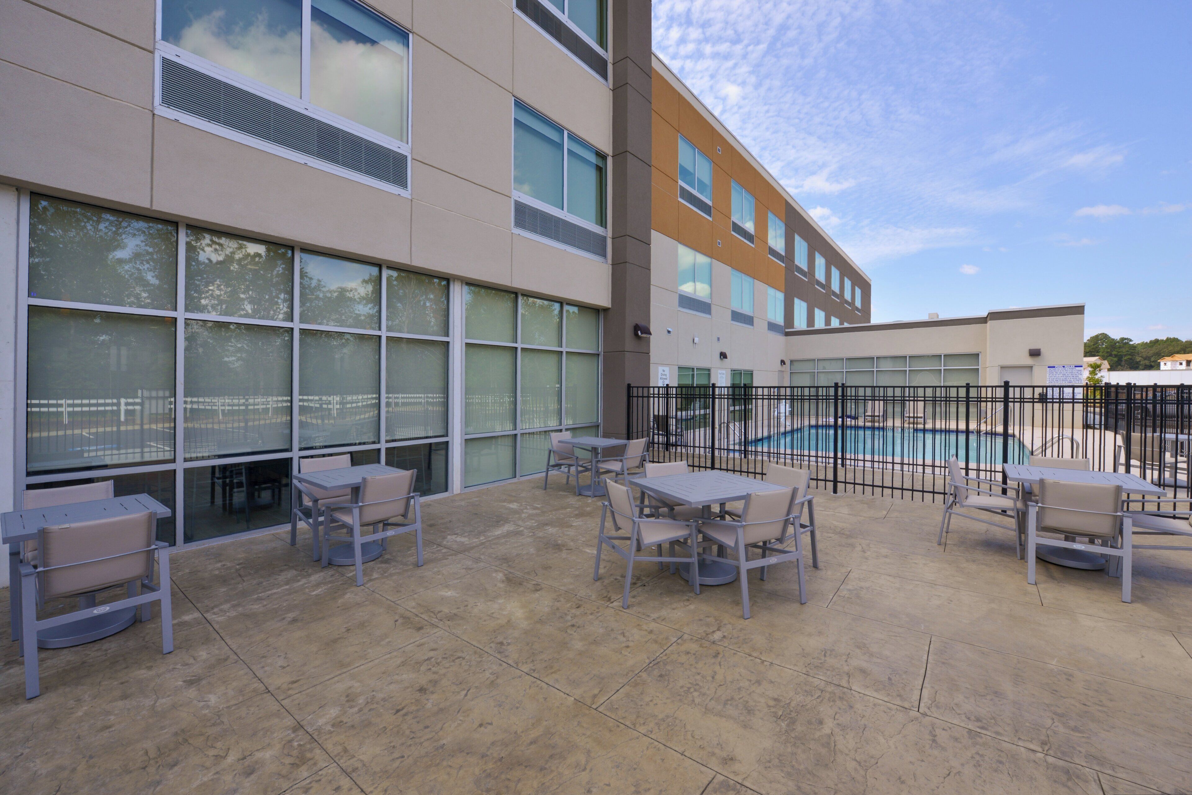 An outdoor patio area with tables and chairs, a swimming pool, and a building with large windows.