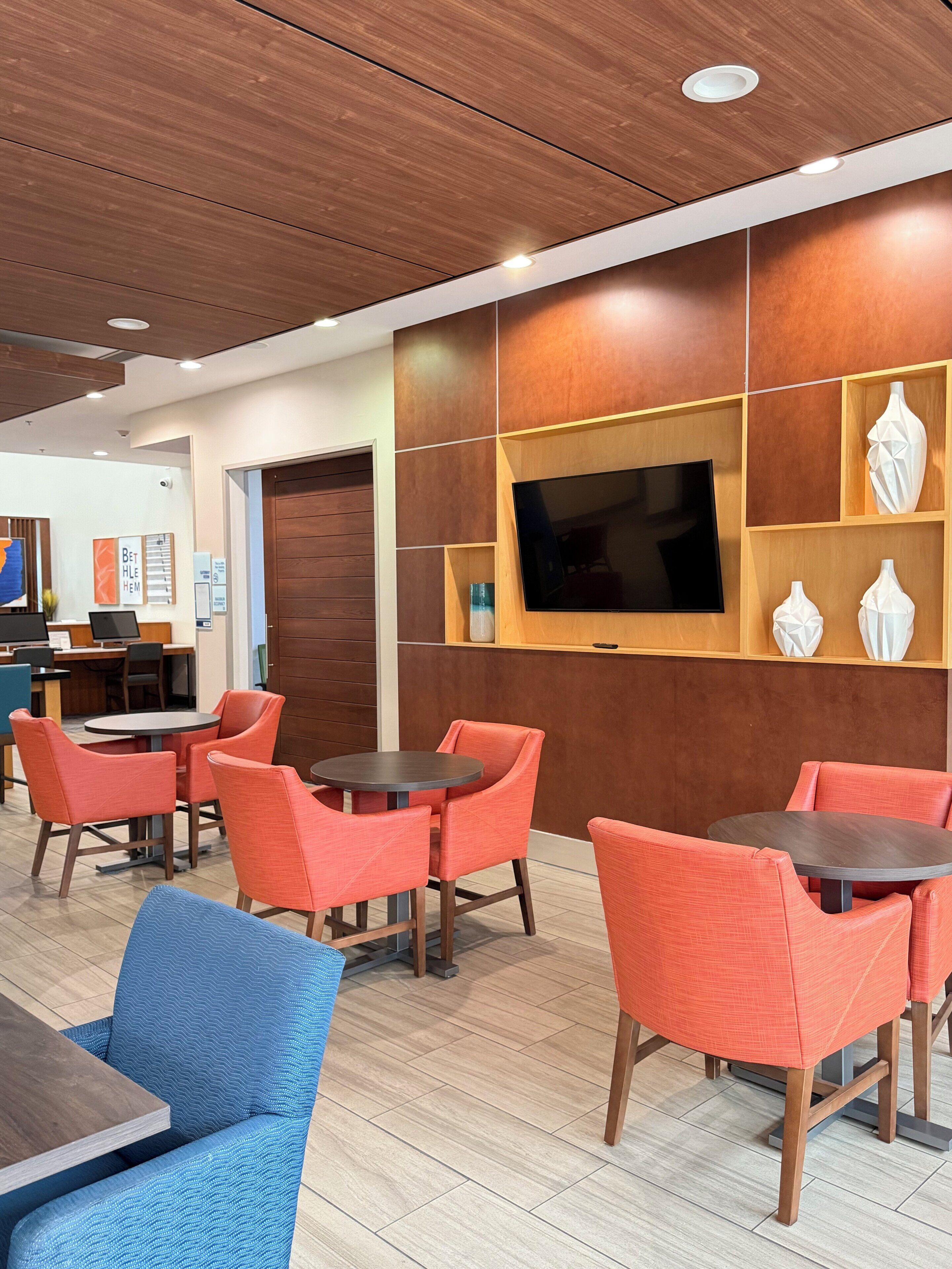 A modern interior with wooden panel walls, a flat-screen TV, and orange and blue upholstered chairs around tables.
