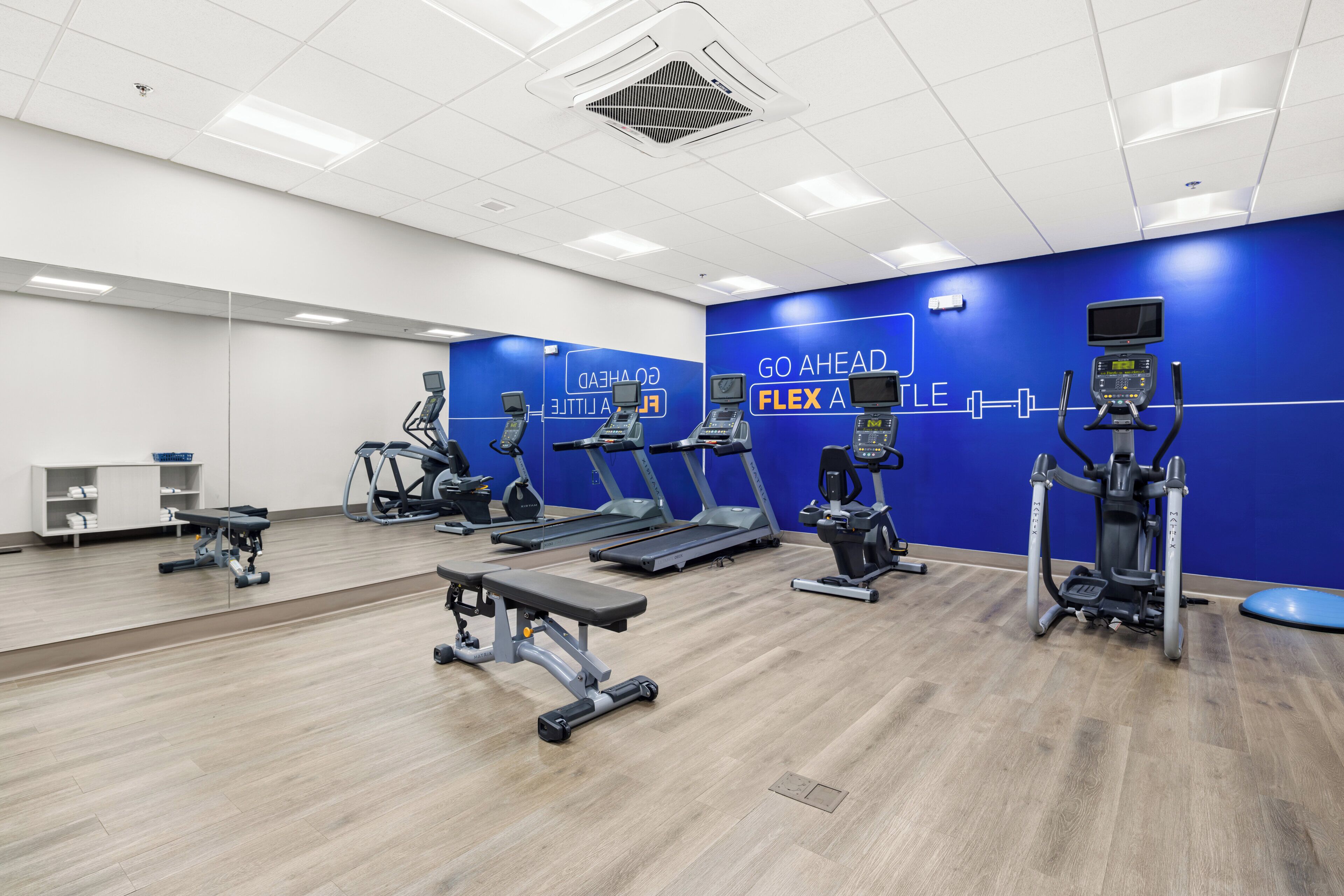 Een sportschool met loopbanden, elliptische trainers en een bankje.