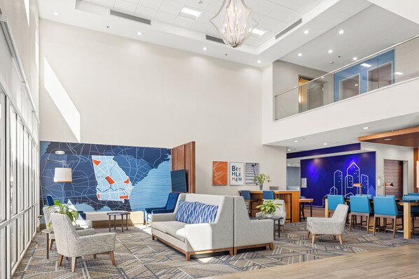 A modern hotel lobby with a high ceiling, a map mural, seating area, and a dining space. - Holiday Inn Express - Bethlehem by IHG (Bethlehem)