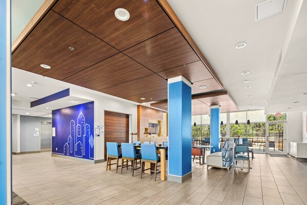 A modern hotel lobby with a wooden ceiling, a reception desk, blue chairs, and a dining area with tables and chairs. - Holiday Inn Express - Bethlehem by IHG (Bethlehem)