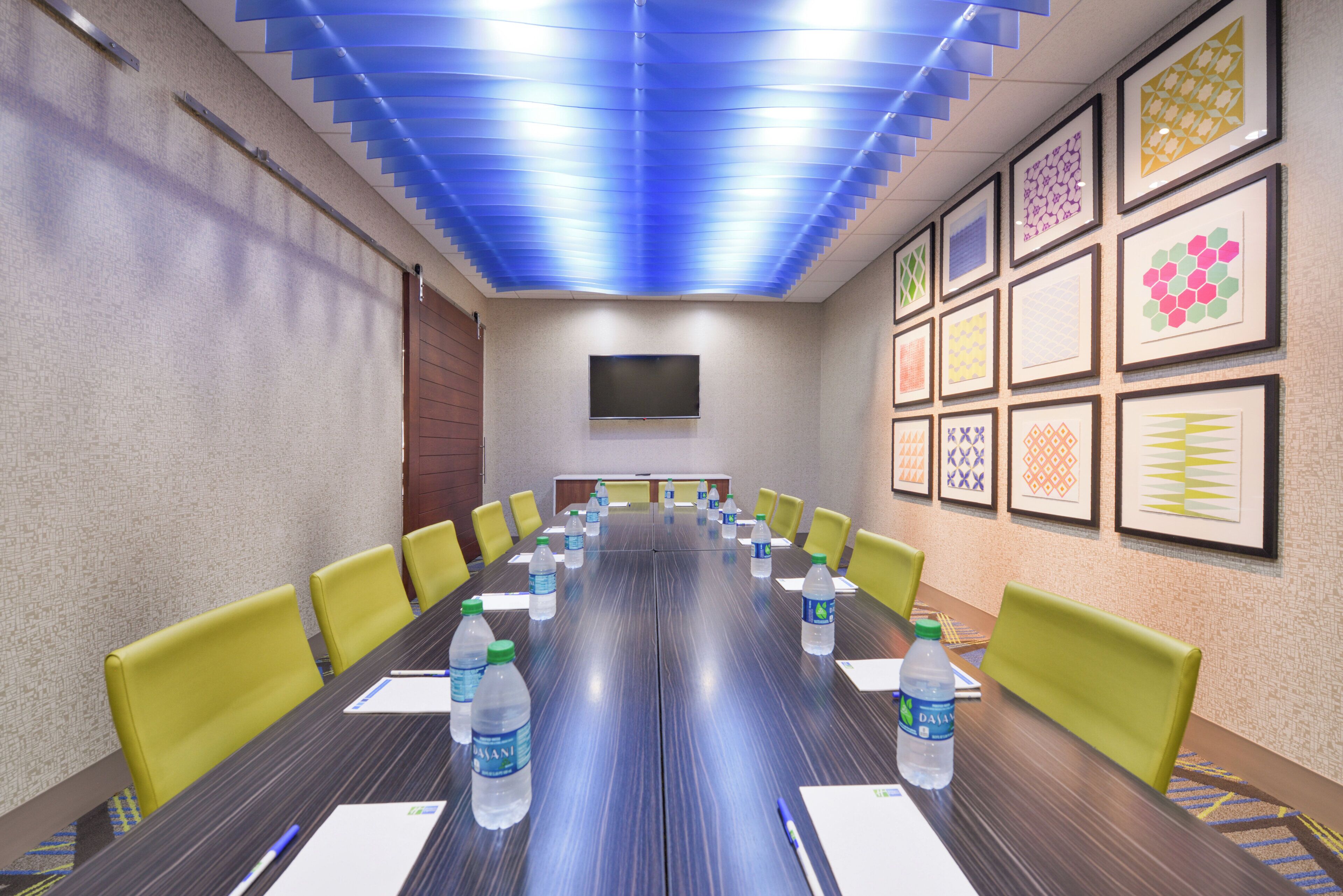 A conference room with a long table, yellow chairs, water bottles, and framed artwork on the walls.
