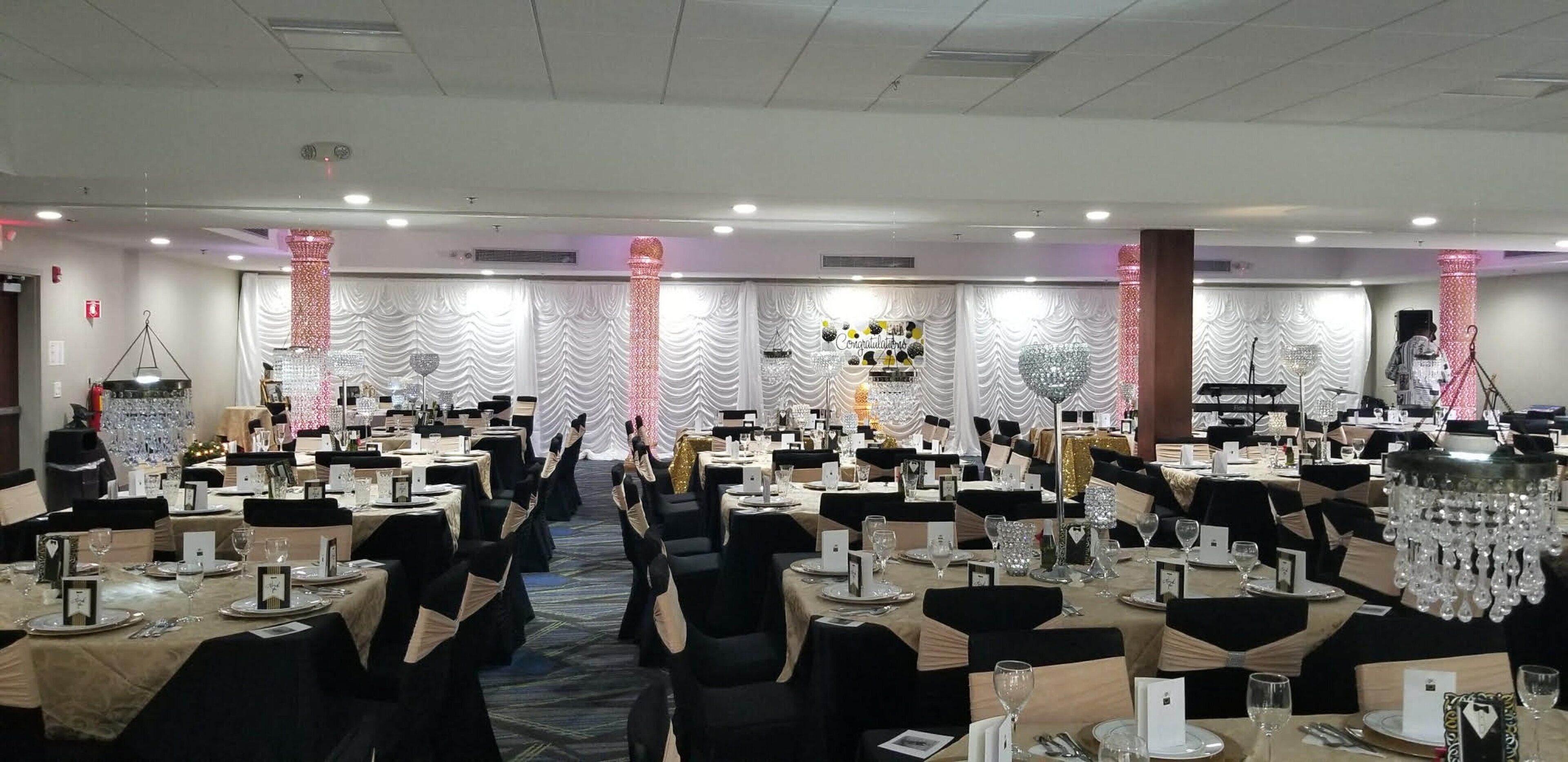 A banquet hall with round tables, black chairs, and white tablecloths.
