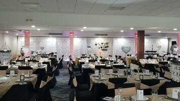 Un salón de banquetes con mesas redondas, sillas negras y manteles blancos.