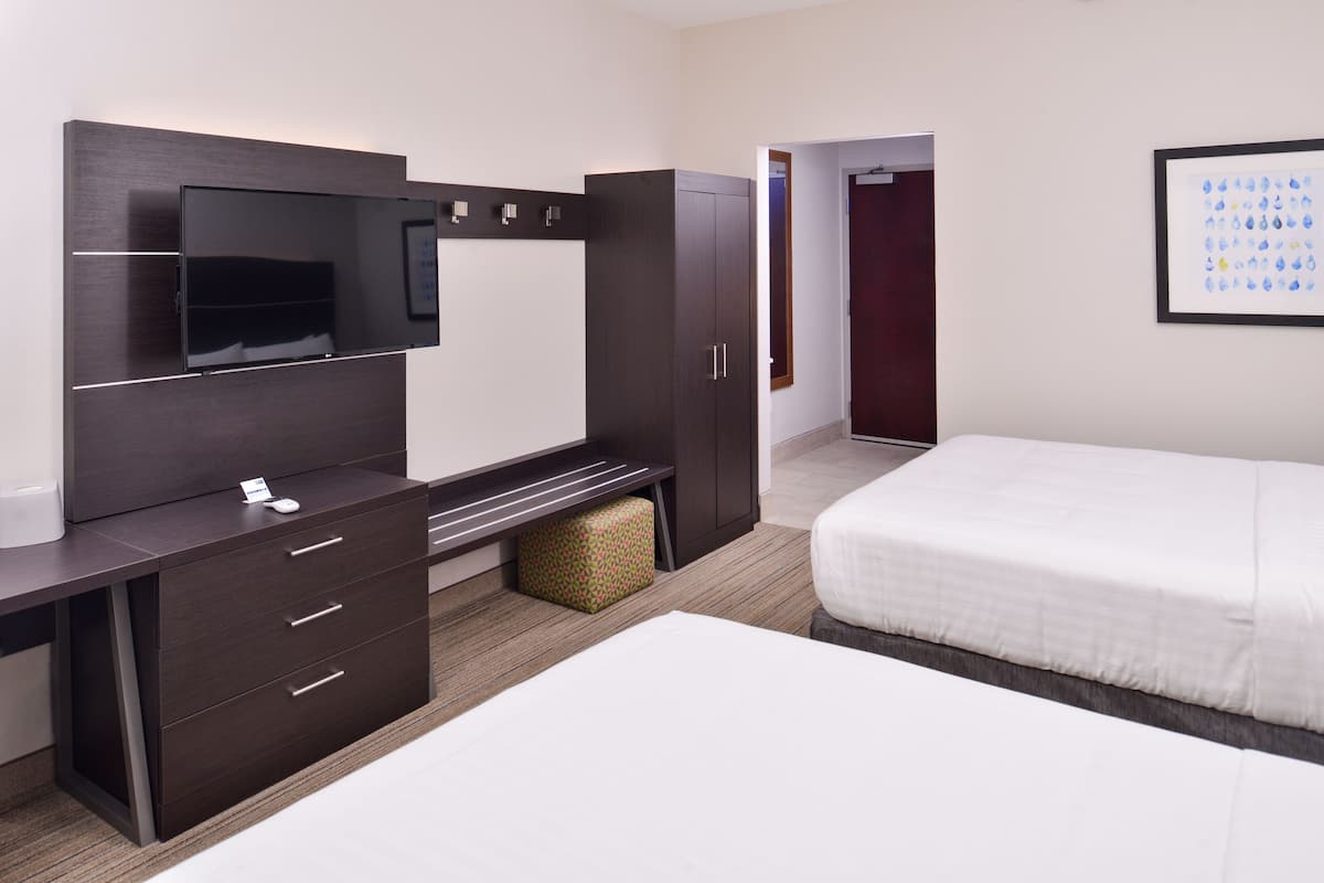 A hotel room with a bed, a desk with drawers, a television, and a wardrobe.
