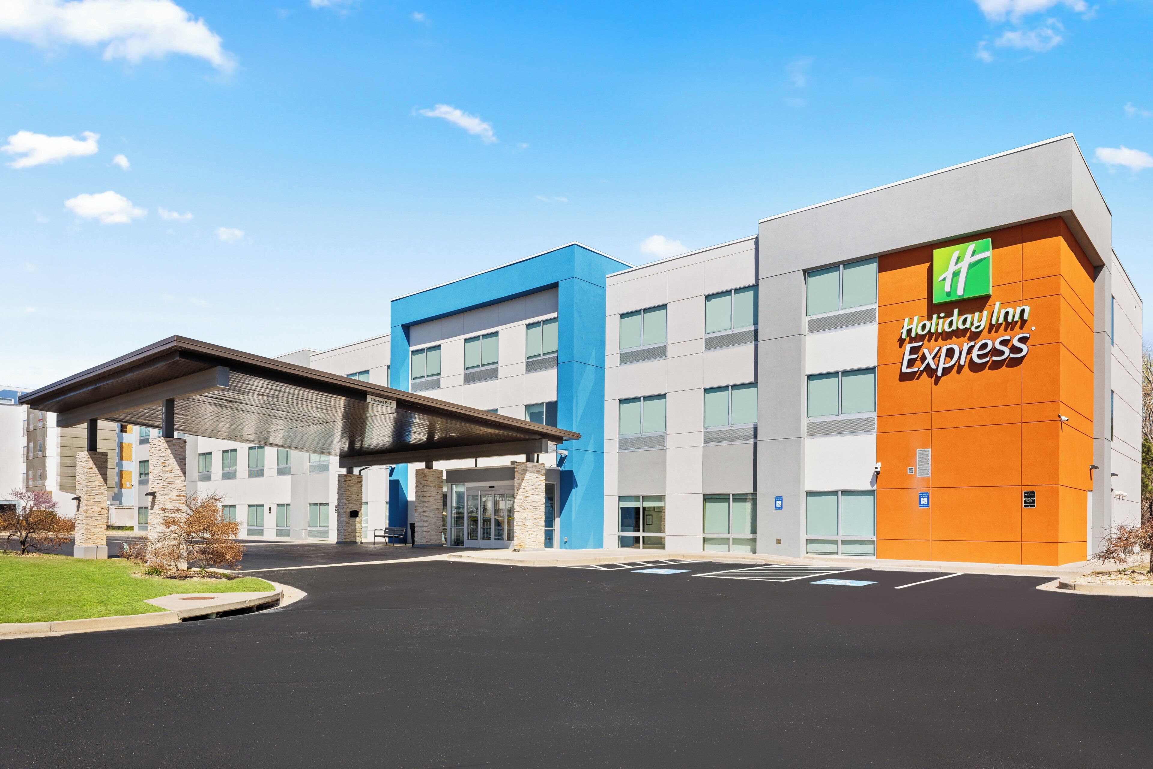 A Holiday Inn Express building with a modern design, featuring a prominent orange and blue color scheme, a covered entrance, and a parking lot.