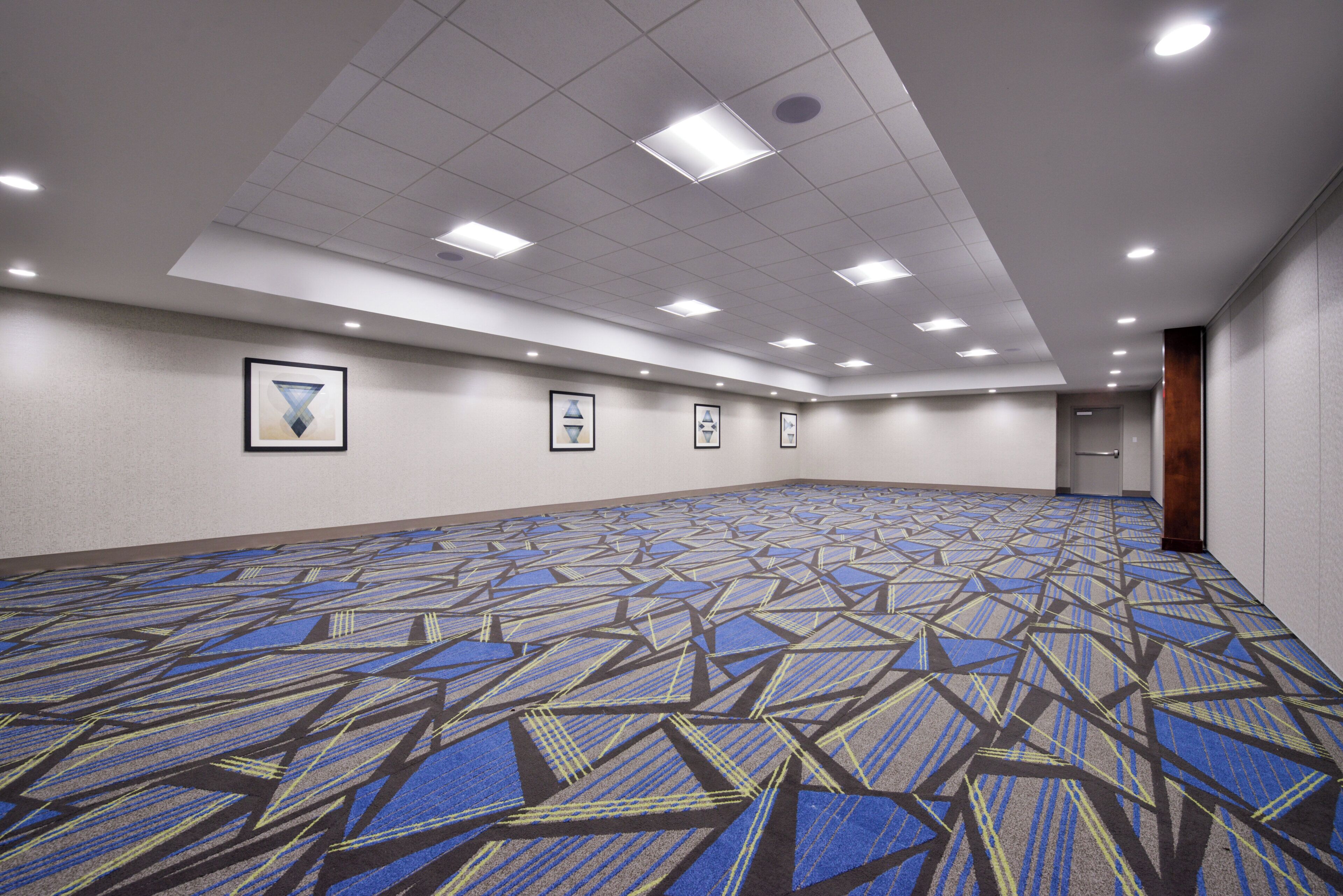 A large, empty conference room with a patterned carpet, recessed ceiling lights, and framed artwork on the walls.