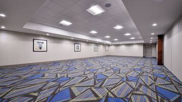 A large, empty conference room with a patterned carpet, recessed ceiling lights, and framed artwork on the walls.