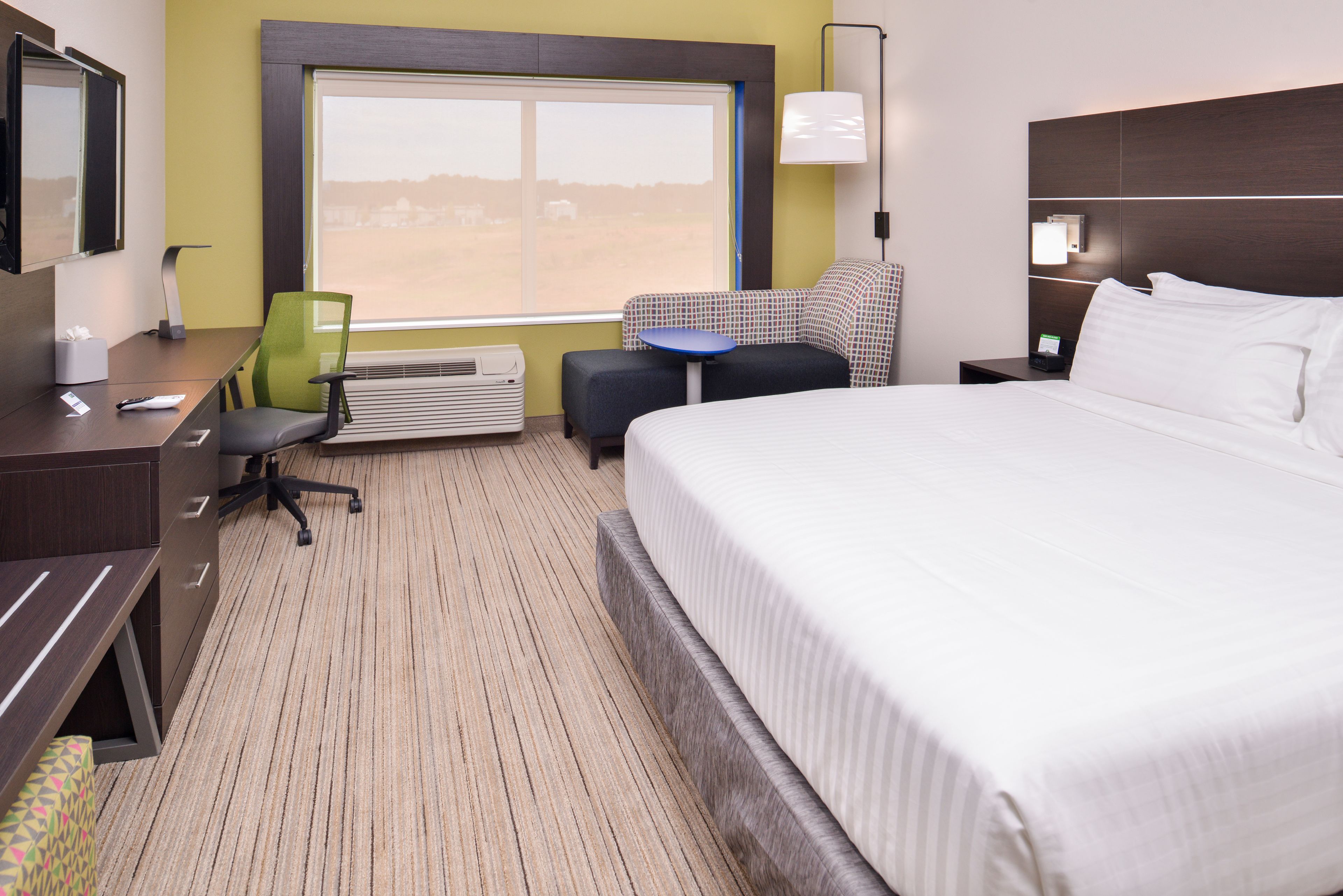 Habitación de hotel con una cama grande, un escritorio con una silla, una mesita pequeña y una ventana con vistas al paisaje.