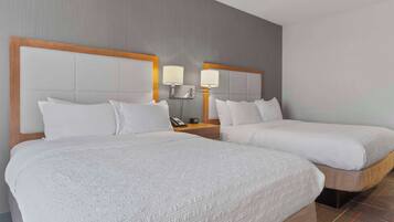 Quarto de hotel com duas camas, uma cabeceira de madeira, uma mesa de cabeceira com abajur e telefone.
