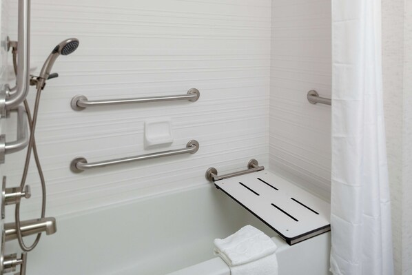 Un baño con ducha, barras de apoyo, toallero y pared de azulejos blancos.