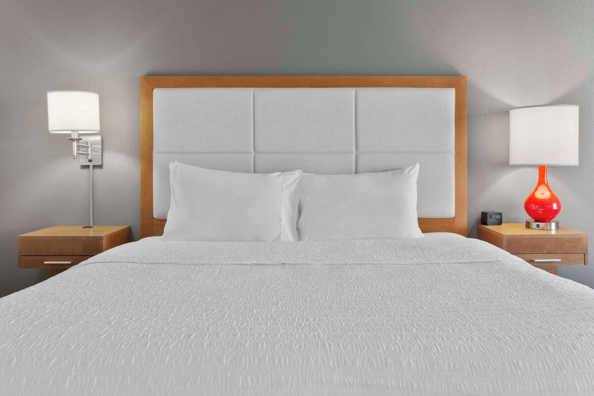 A neatly made bed with a wooden headboard, two bedside tables with lamps, and a wall clock.