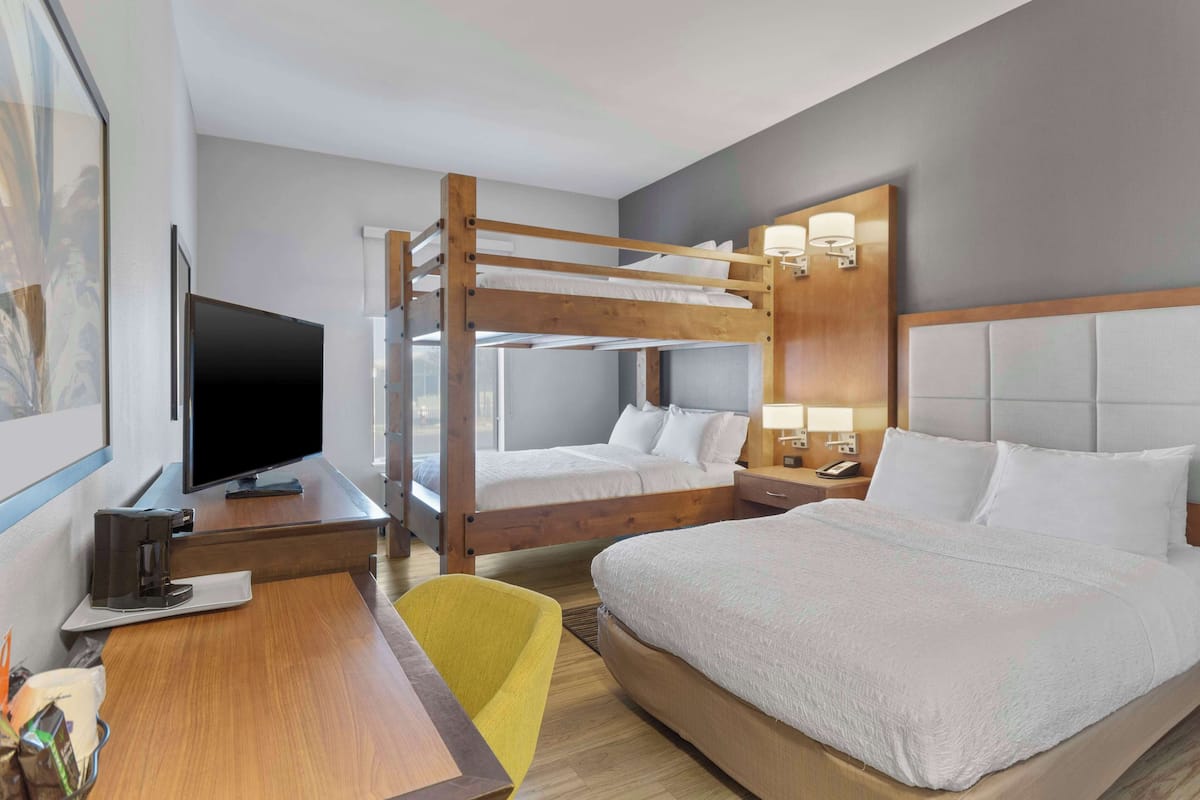 A hotel room with bunk beds, a desk with a television, and a bedside table with a lamp.
