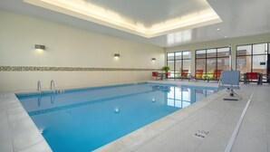 Una gran piscina interior con agua cristalina, rodeada de suelo y paredes con baldosas, y equipada con una silla de salvavidas y señalización de seguridad.
