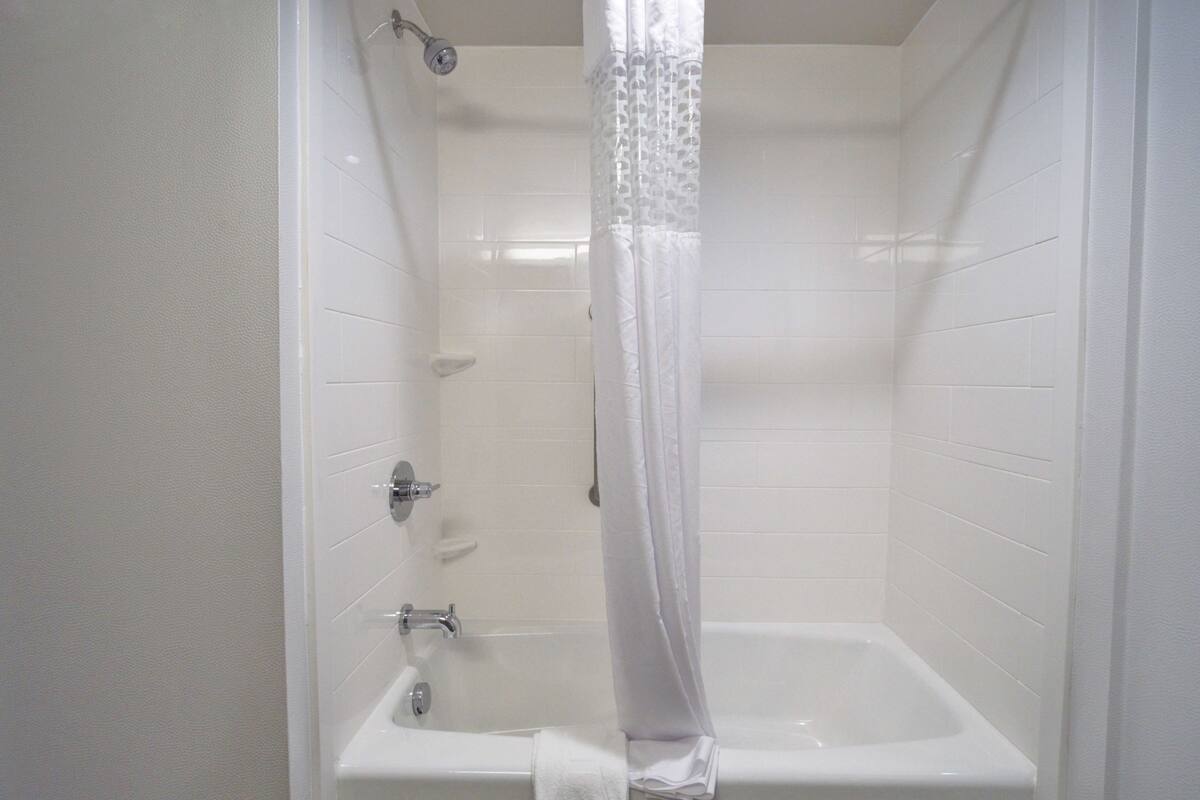 A white bathroom with a bathtub, shower curtain, and white tiles.