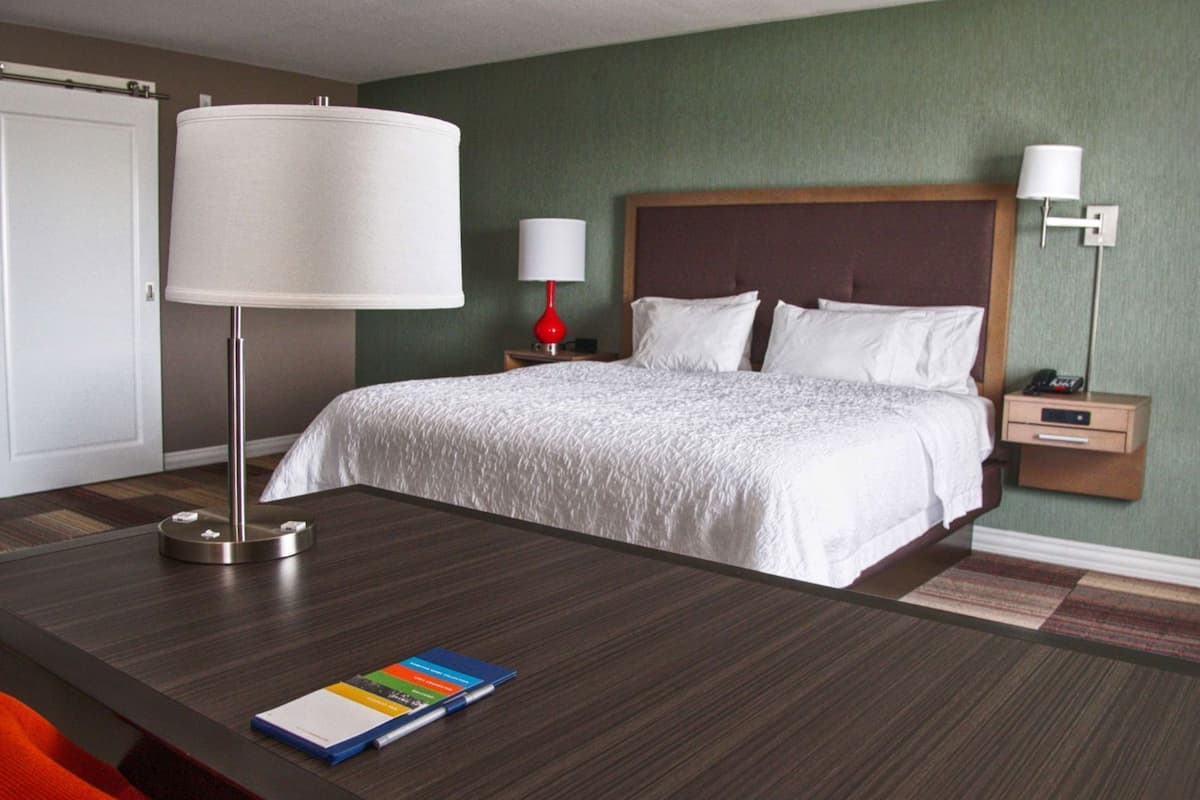 A hotel room with a bed, bedside tables, a desk with a lamp, and a chair.
