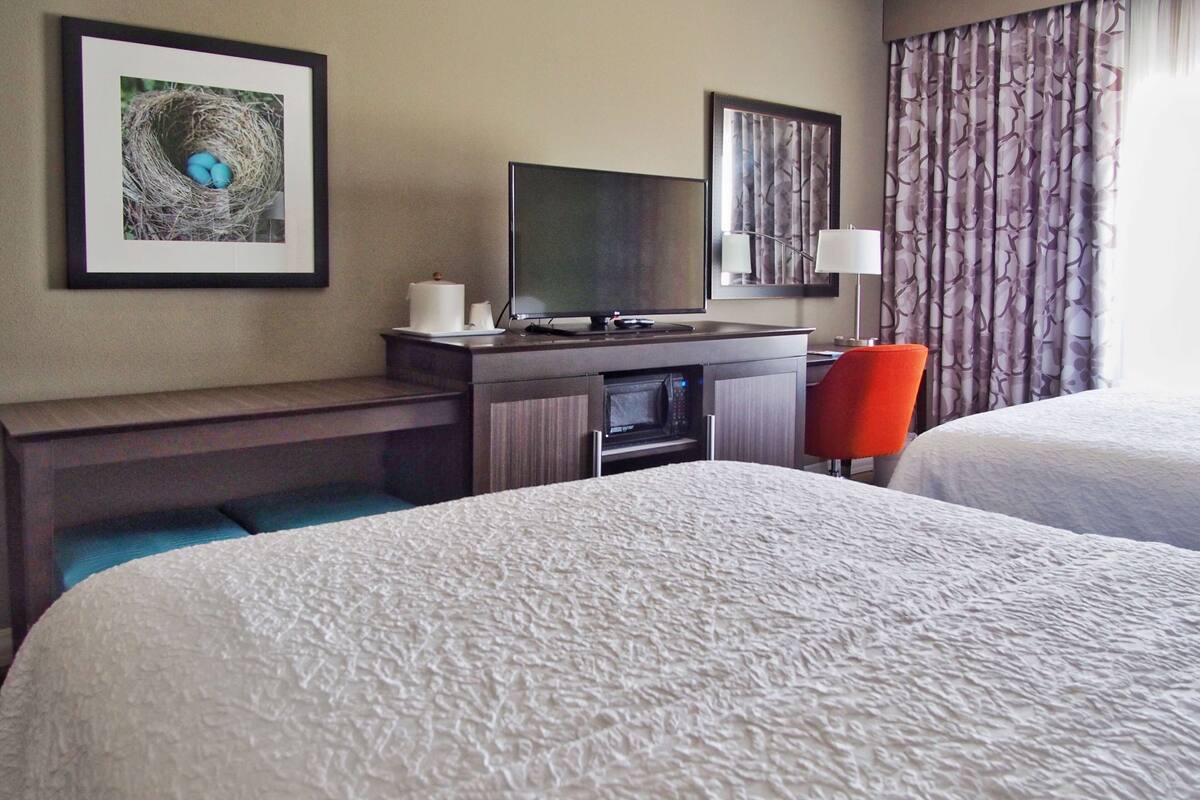 A hotel room with two beds, a desk with a television, a microwave, and a red chair.