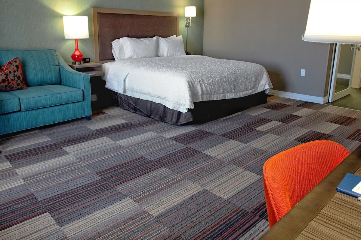 A hotel room with a bed, a blue sofa, an orange chair, and a patterned carpet.