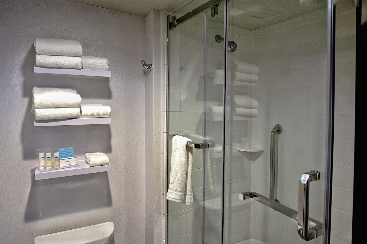 A modern bathroom with a glass shower enclosure, white towels on shelves, and toiletries.
