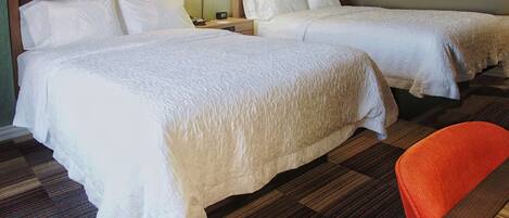 A hotel room with two beds, a nightstand, a lamp, and a chair.