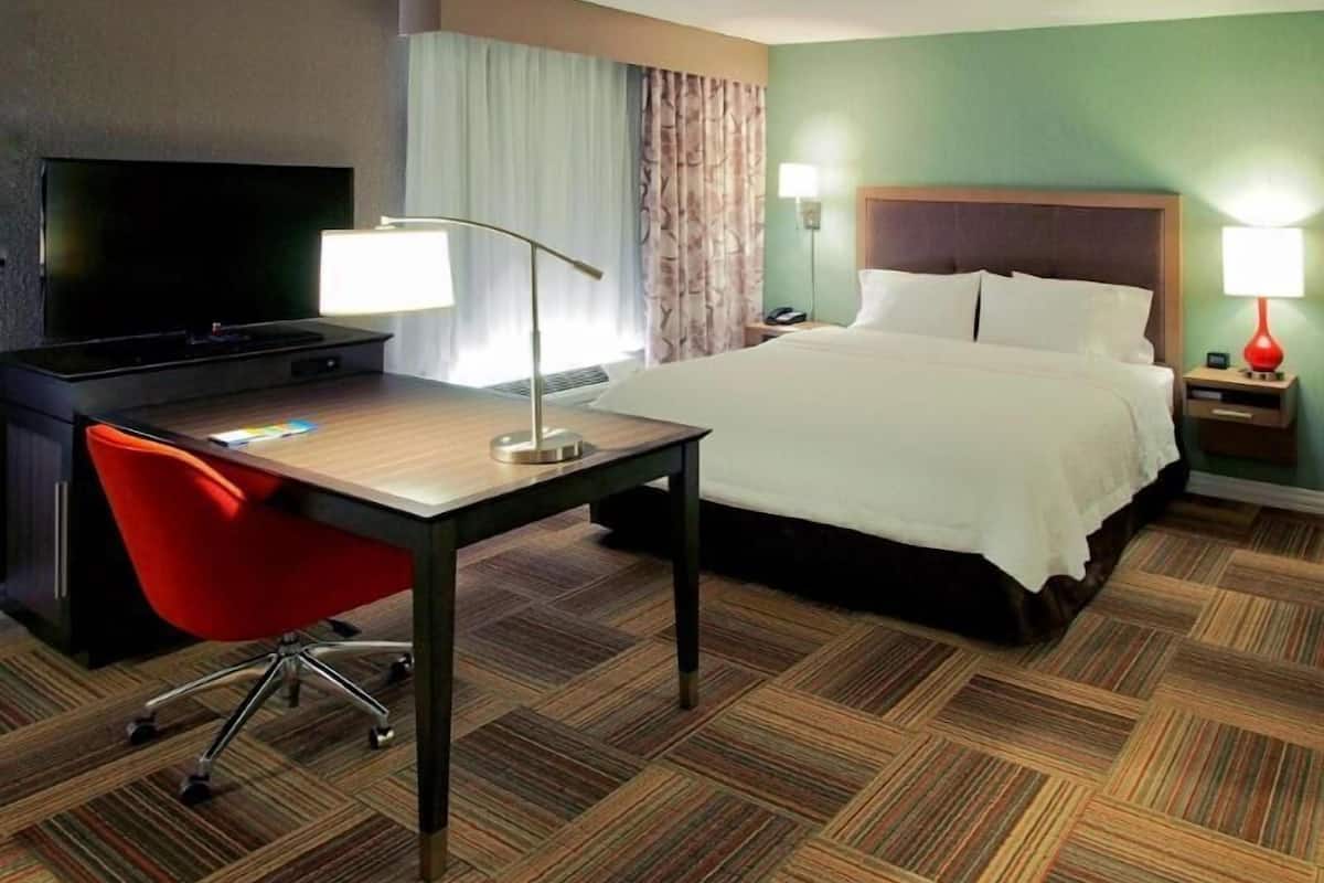 A hotel room with a bed, desk, chair, TV, and lamps.