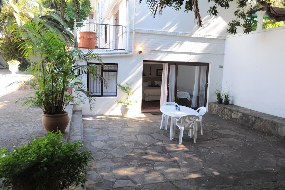 Un patio con suelo de piedra, paredes blancas, un balcón y plantas en macetas.