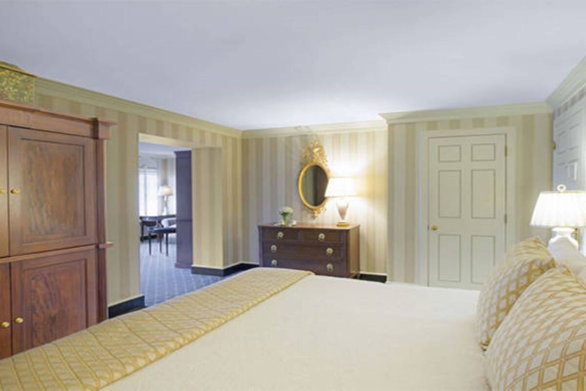 A hotel room with a large bed, a dresser with a mirror, and a door leading to another room.