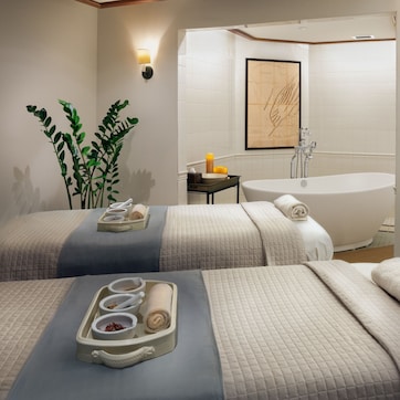A spa room with two massage beds, a bathtub, and a small table with towels and a candle.