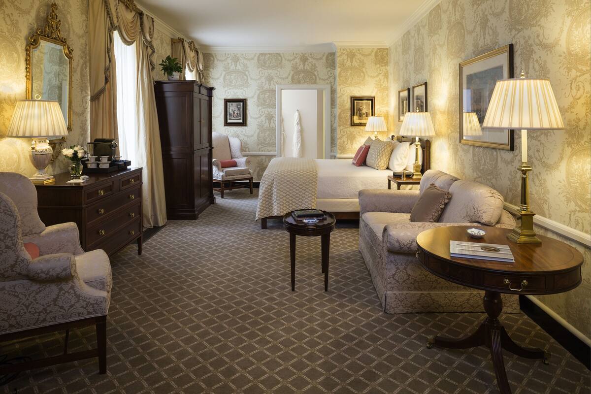 A hotel room with a bed, two armchairs, a sofa, a small table, a cabinet, and two lamps.