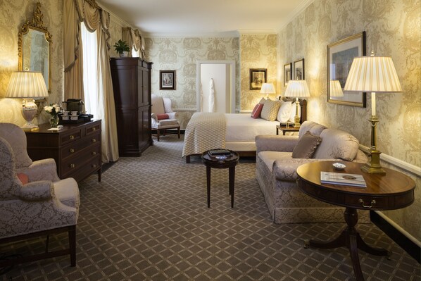 Habitación de hotel con cama, dos sillones, sofá, mesita, armario y dos lámparas.