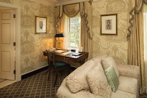 A room with a desk, chair, and a sofa. There are two framed pictures on the wall.