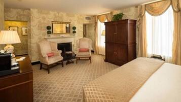 Une chambre d’hôtel comprenant un lit, deux fauteuils, une cheminée, une armoire et une lampe.