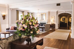 A hotel lobby with a large floral arrangement on a wooden table, a sofa, a fireplace, and a chandelier. - Williamsburg Inn, an official Colonial Williamsburg Hotel (Williamsburg)