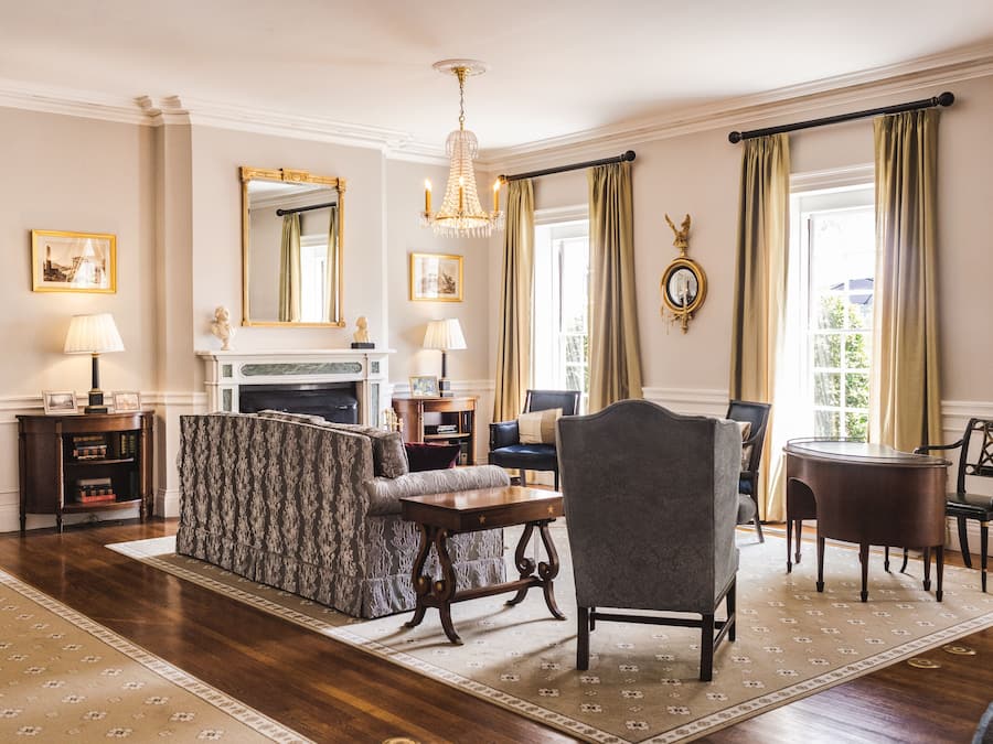 A formal living room with a fireplace, a chandelier, and a dining area with a round table and chairs.