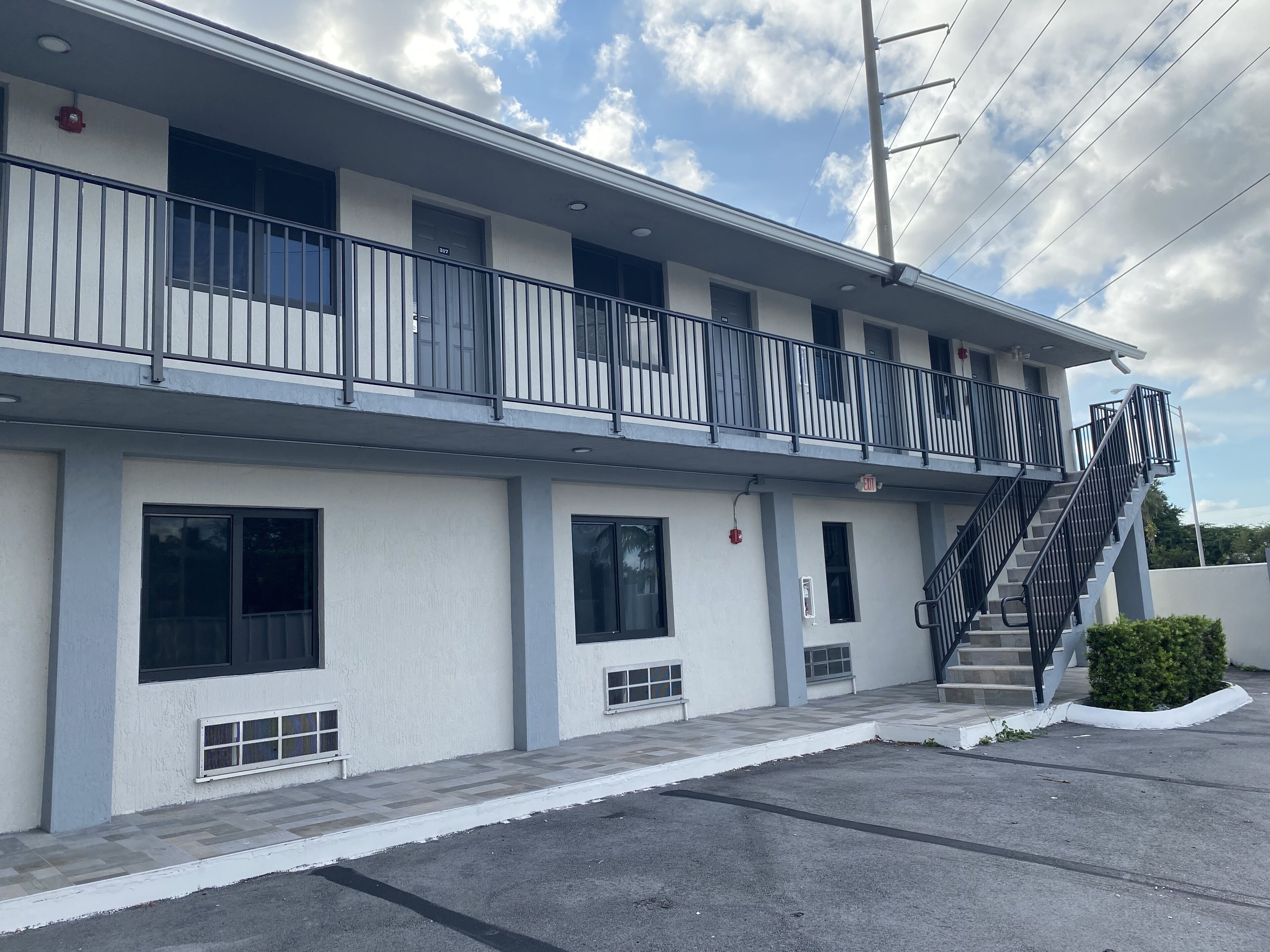 A two-story motel with a flat roof, multiple windows, a covered outdoor area, and a staircase leading to the upper floor.