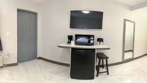 Ein Hotelzimmer mit Flachbildfernseher an der Wand, kleinem Kühlschrank, Kaffeemaschine und Spiegel.