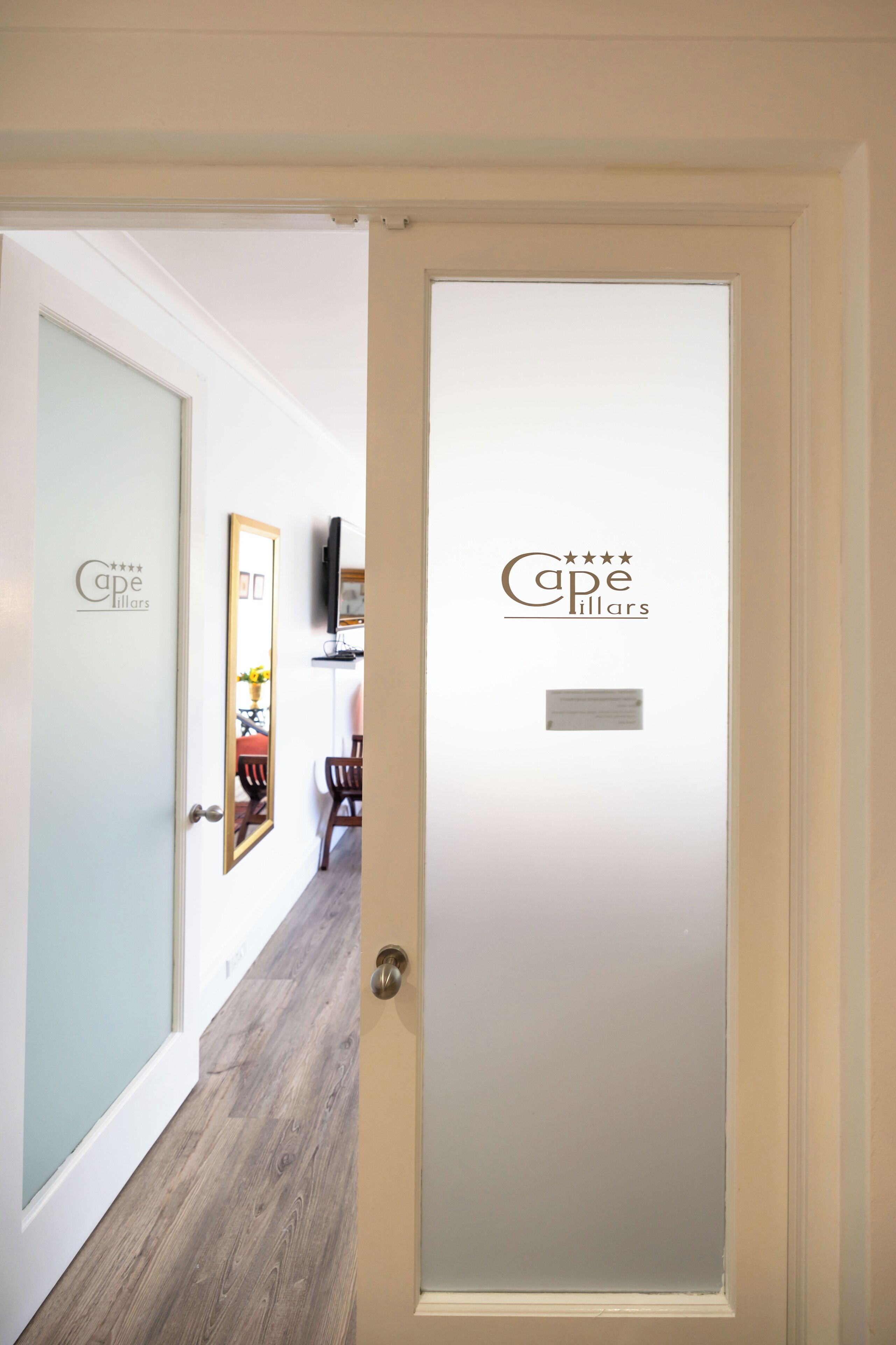 A hotel entrance with a frosted glass door, a sign reading "Cape Pillars," and a wooden floor.