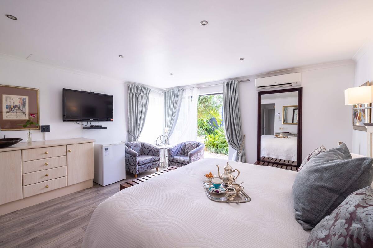 Ein Hotelzimmer mit Bett, Fernseher, Schreibtisch, Stuhl und einem Fenster mit Vorhängen.