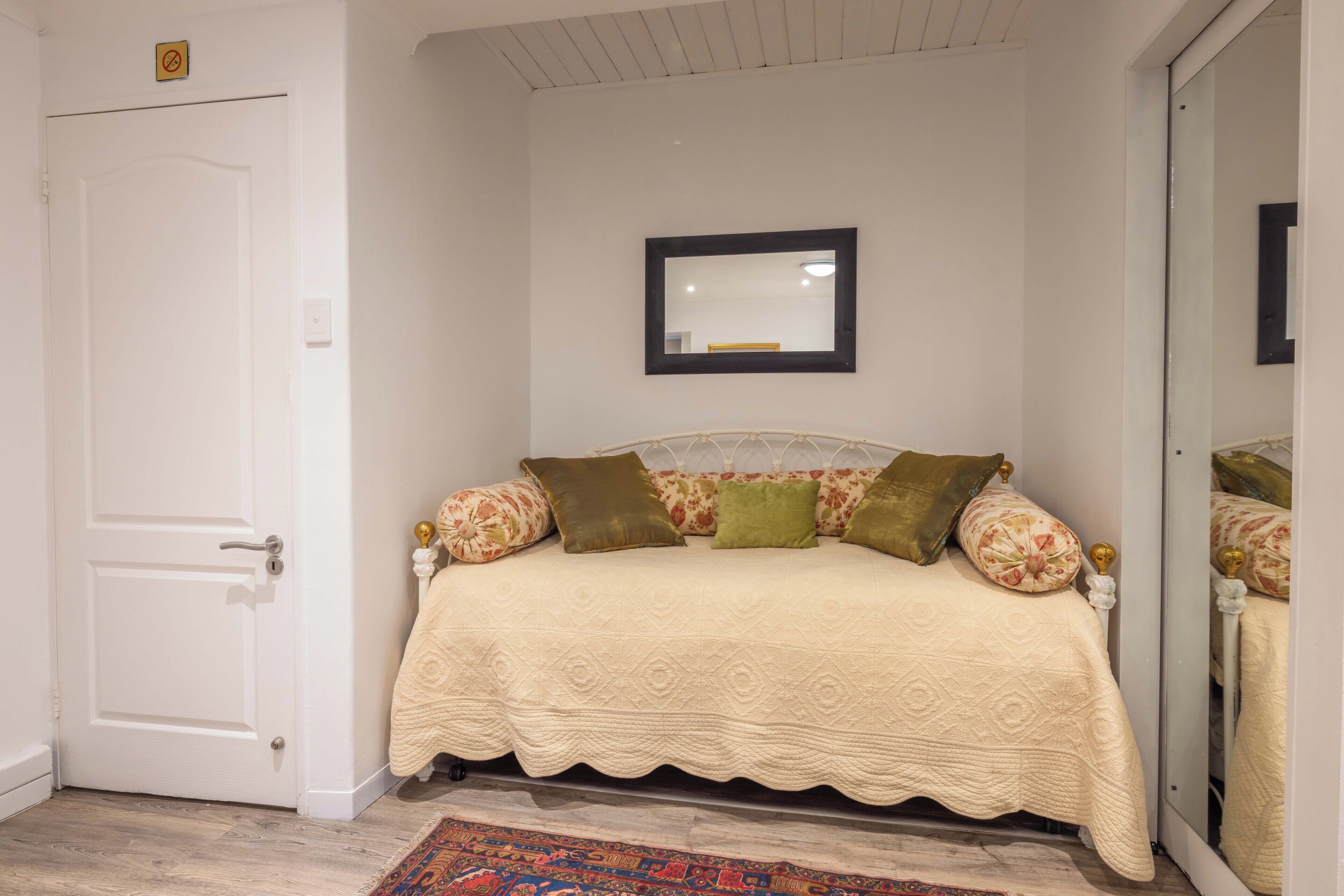 Un dormitorio con cama, puerta, espejo y alfombra estampada.