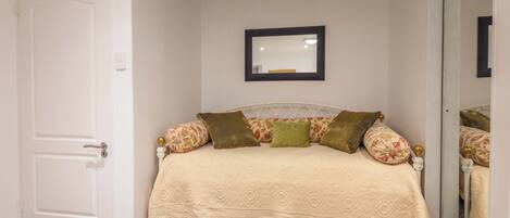 Un dormitorio con cama, puerta, espejo y alfombra estampada.