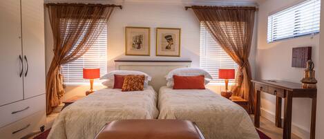 A double bedroom with two beds, a nightstand, a dresser, and a desk.