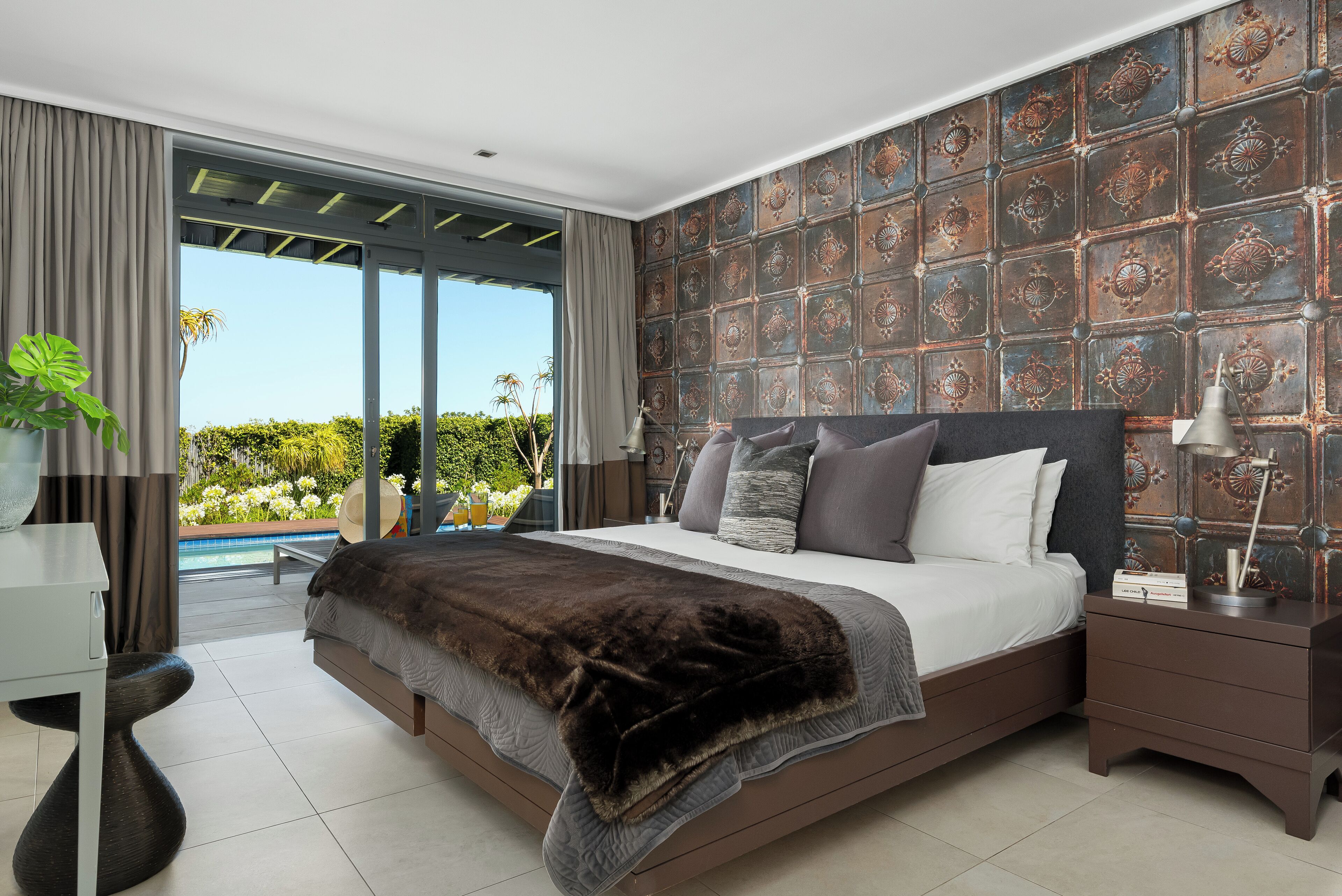 A modern bedroom with a large bed, a view of a swimming pool, and a decorative wall.