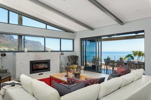 A modern living room with a fireplace, large windows, and a view of the ocean. - Hely Horizon (Cape Town)